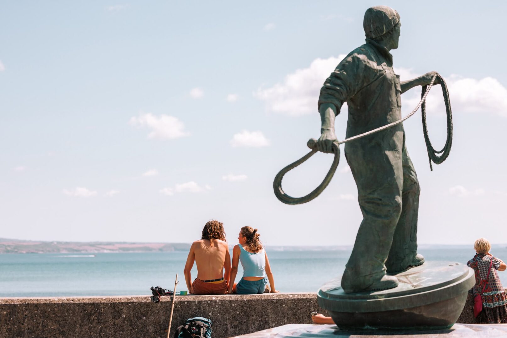 Visitors pausing beside a coastal statue on the path
