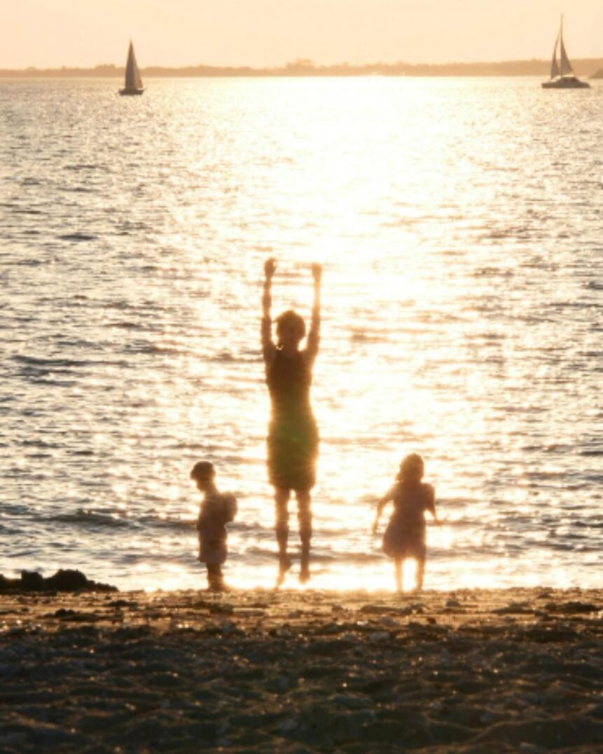 Children playing on a beach at sunset with sailboats