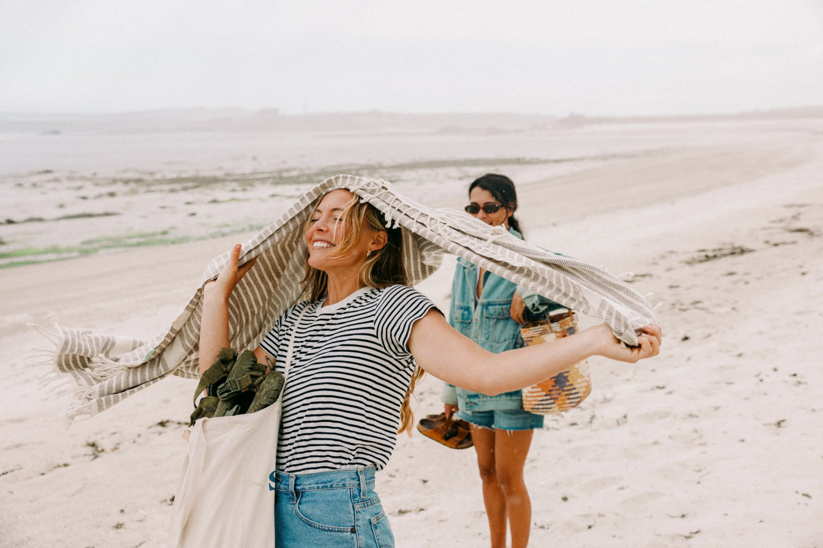 Two women on a Cornish beach holding a blanket over their heads