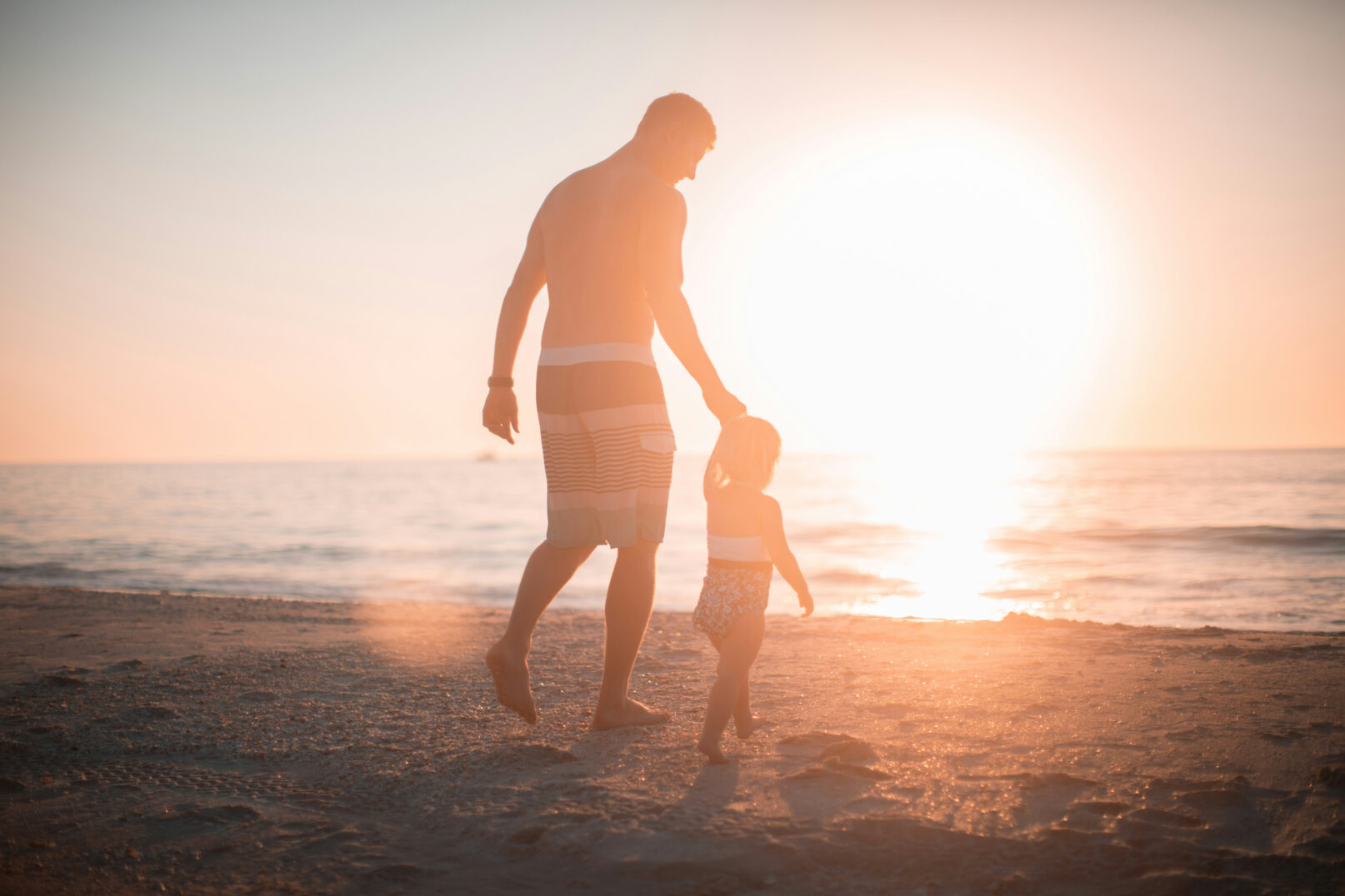 Father and child walking on the beach at sunset